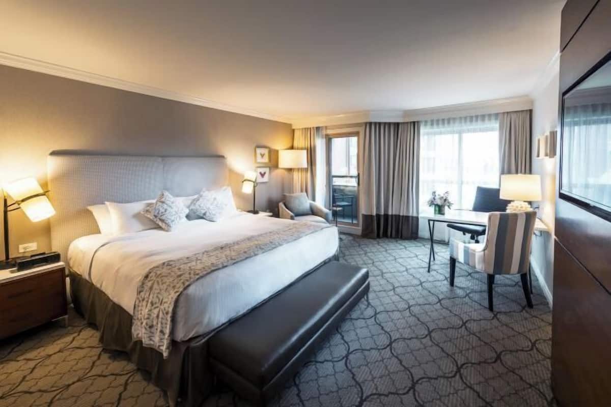 A hotel room with a large bed, bedside tables, a desk, and a view of the city.