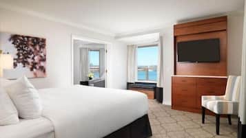A hotel room with a large bed, a TV mounted on a wooden cabinet, a chair, and a view of the outdoors.