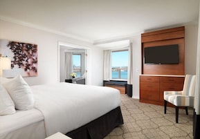 Habitación de hotel con una cama grande, un televisor instalado en un mueble de madera, una silla y vistas al exterior.