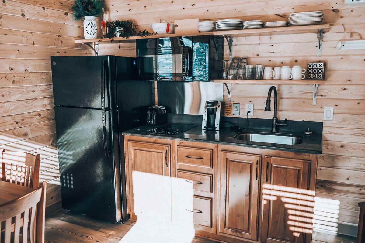 A kitchen with wooden cabinets, a black refrigerator, a microwave, and a sink.