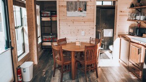 Un interior de madera con una mesa redonda de comedor, sillas, una zona de cocina con armarios y un extintor.