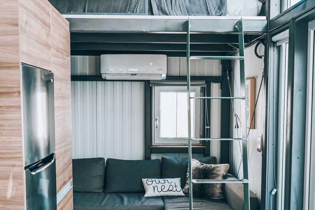 A compact living space with a bunk bed, kitchenette, and a sofa with cushions.