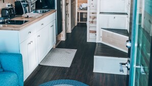 Interior de cabaña de madera, compacto, con kitchenette, comedor y escalera que lleva a un nivel superior.
