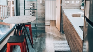 Una cocina moderna con suelo de madera, un comedor con taburetes rojos y vistas a través de un ventanal grande.