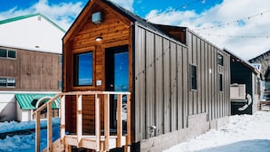Una cabaña de madera con un porche y una extensión metálica, rodeada de nieve.