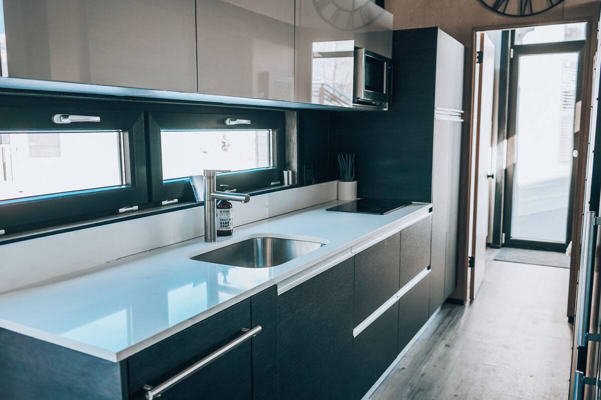 A modern kitchen with a stainless steel sink, dark cabinets, and a window overlooking the street.