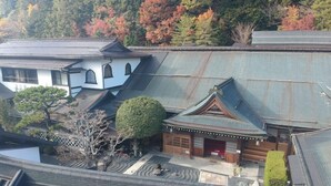 A traditional Japanese building with a curved roof, surrounded by trees with autumn foliage. - Sekishoin (Koya)