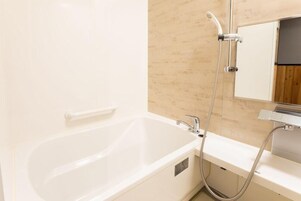 Un baño moderno con una bañera blanca, un cabezal de ducha manual y un espejo sobre el lavabo.