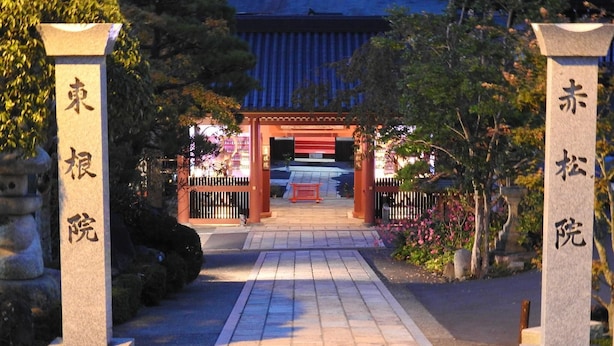 A traditional Japanese gate with stone pillars and a tiled pathway leading to a building with a red roof. - Sekishoin (Koya)