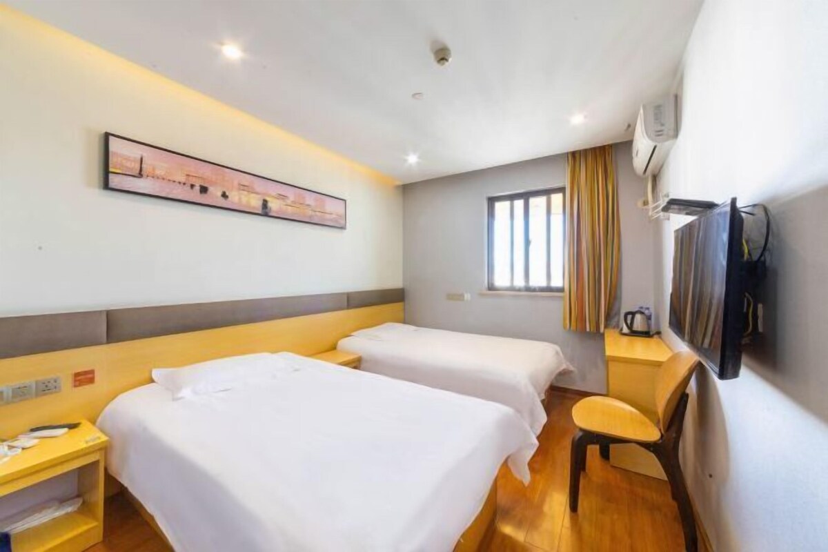 Ein Hotelzimmer mit zwei Betten, einem Schreibtisch, einem Stuhl, einem Fernseher und einem Fenster mit Vorhängen.