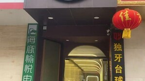Ein Hotelzugang mit einem grünen Schild, einem roten Laternenfächer und einem großen, runden Schild über der Tür.