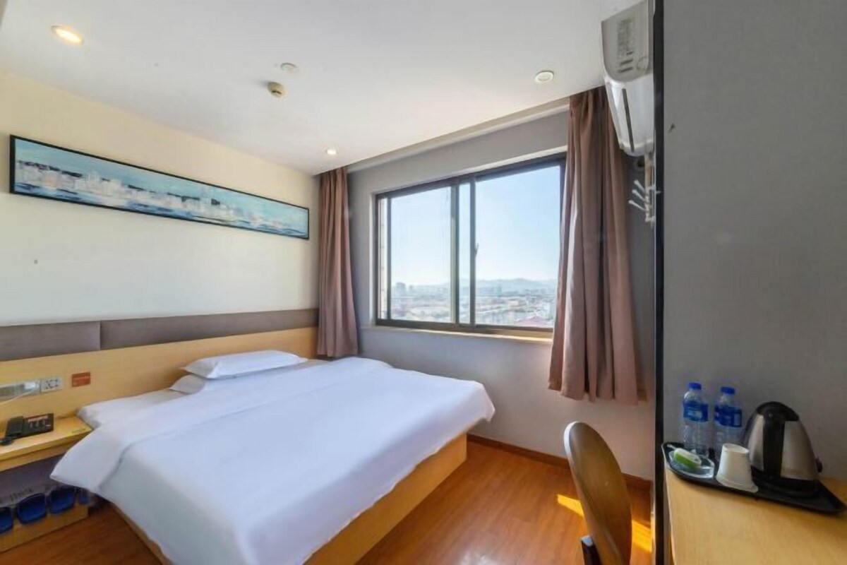 Ein Hotelzimmer mit Bett, Schreibtisch mit Stuhl, Fenster mit Stadtblick und einem Bild an der Wand.