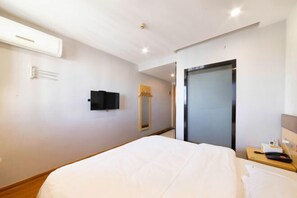 Ein Hotelzimmer mit einem Bett, einem Nachttisch mit Telefon und Lampe, einem an der Wand montierten Fernseher und einer Tür mit Milchglasfenster.