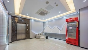 Eine moderne Lobby mit Marmorboden, einem roten Getränkeautomaten, einer Couch und einem Aufzug.
