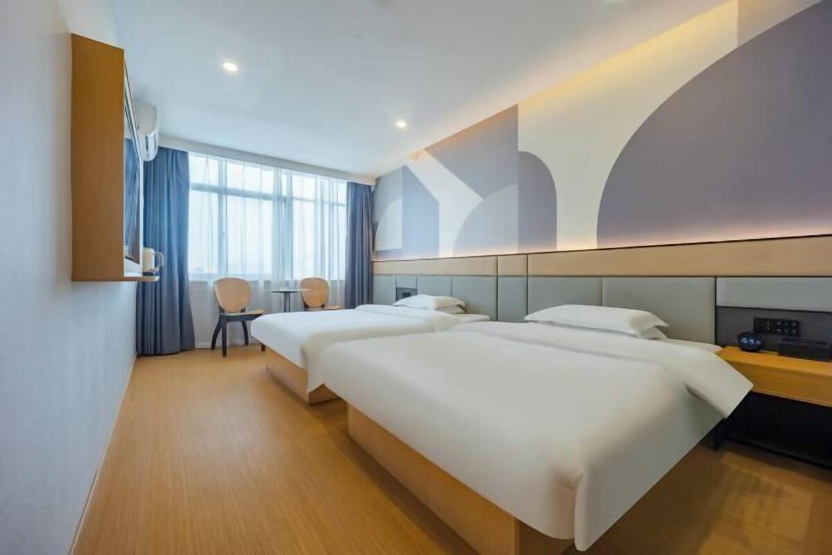 A hotel room with two beds, a desk, a chair, and a large window.