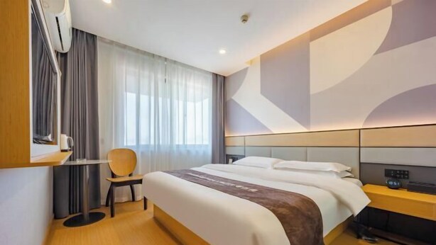 Ein modernes Hotelzimmer mit einem großen Bett, einem Nachttisch, einem Sessel und einem Fenster mit Vorhängen.