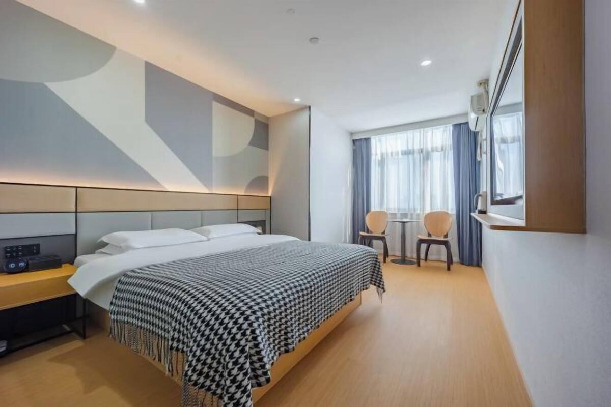 A modern hotel room with a large bed, bedside table, and a small seating area with a table and chairs.