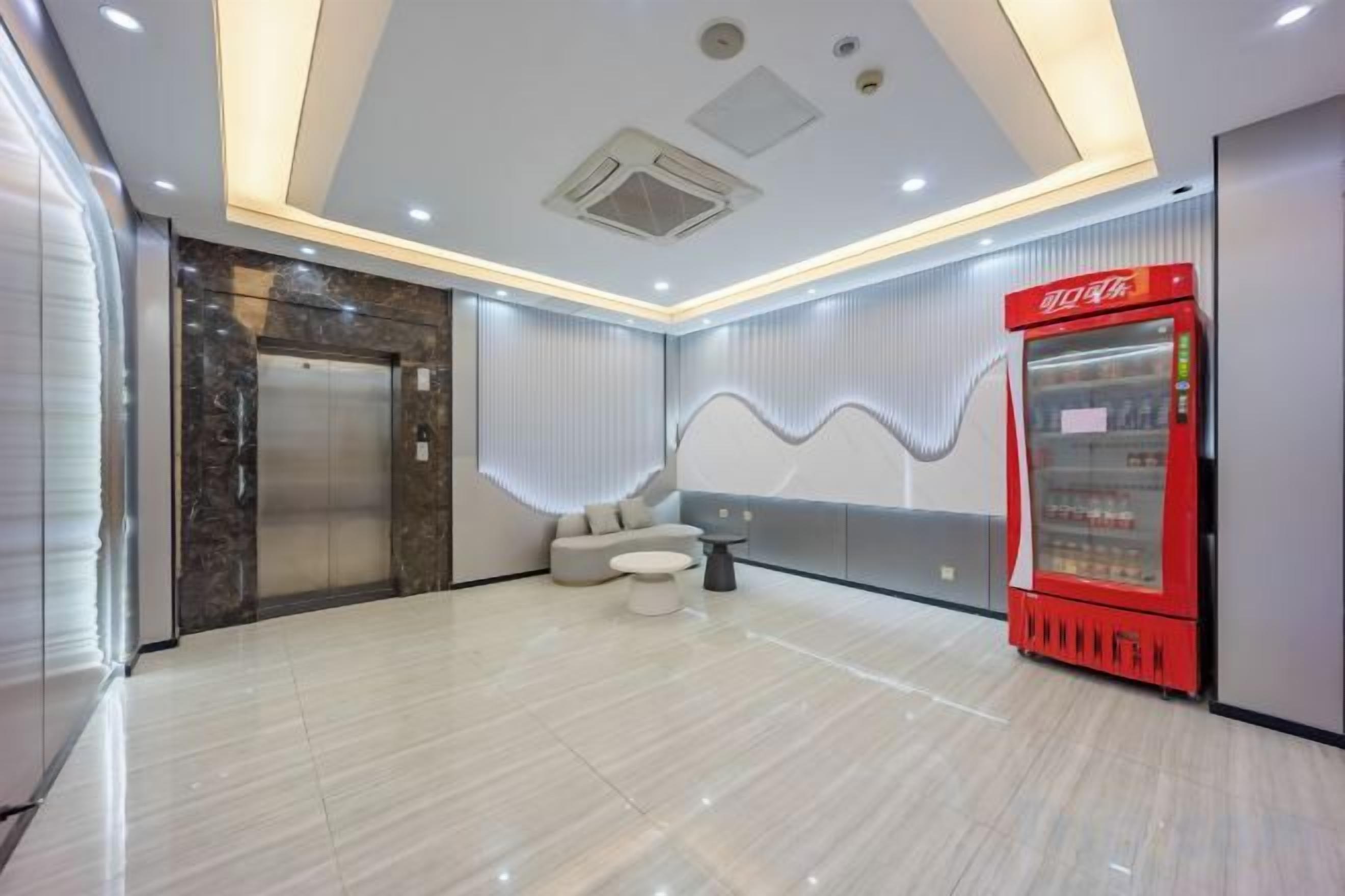 A hotel lobby with a marble floor, a red vending machine, a seating area, and a modern elevator.