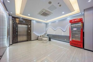 A hotel lobby with a marble floor, a red vending machine, a seating area, and a modern elevator.