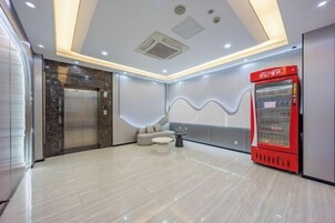 Um saguão de hotel com piso de mármore, uma máquina de vendas vermelha, uma área de estar e um elevador moderno.