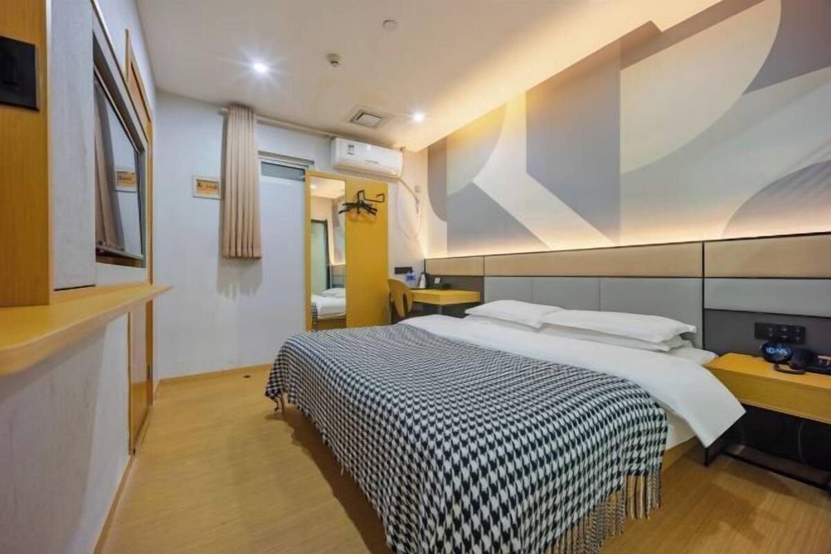 A modern hotel room with a large bed, a bedside table, a mirror, and a wall-mounted air conditioning unit.