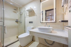 Un baño moderno con ducha envuelta en vidrio, inodoro blanco, lavamanos de mármol y un espejo grande.
