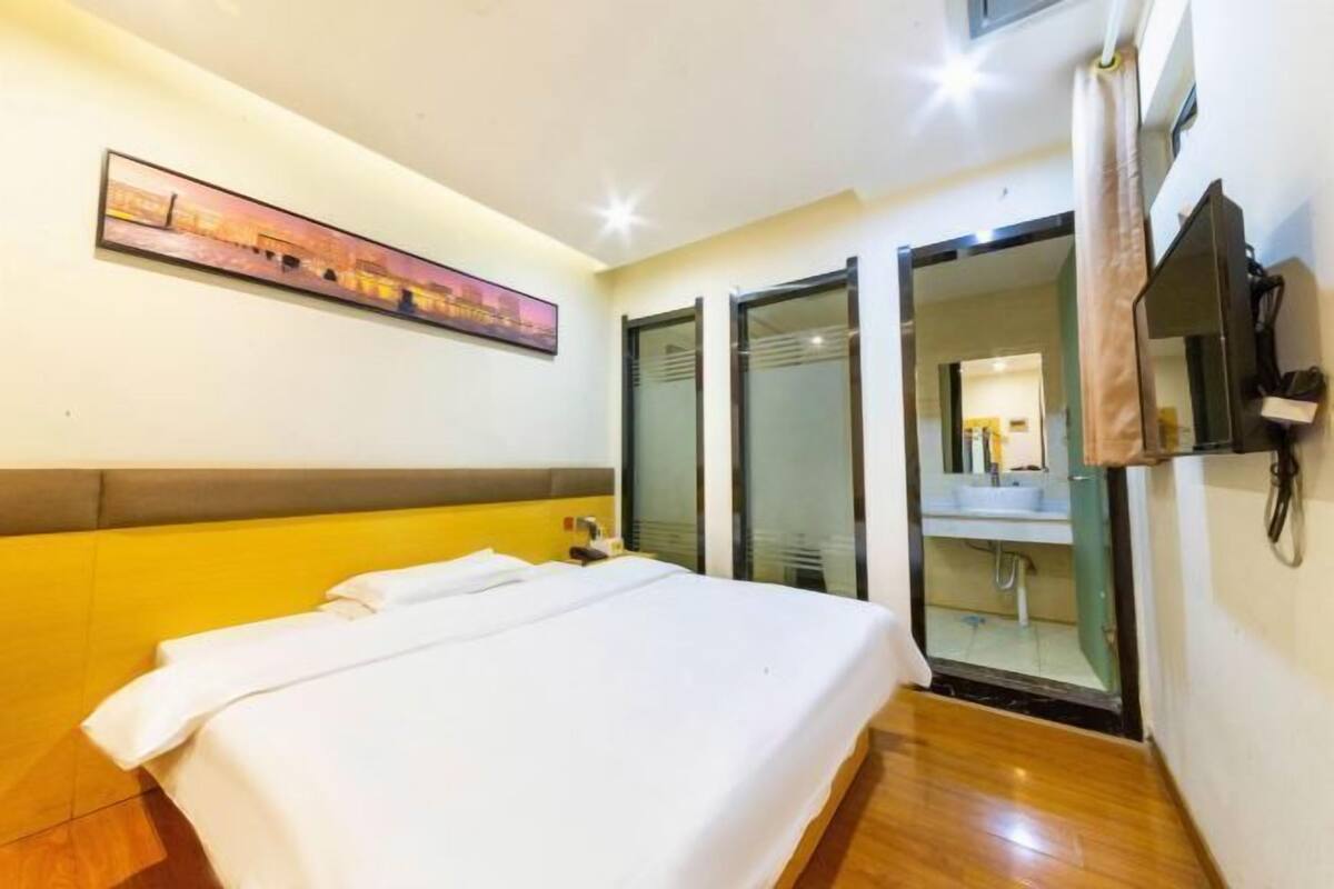 A hotel room with a bed, a painting on the wall, a sliding door to the bathroom, and a TV mounted on the wall.