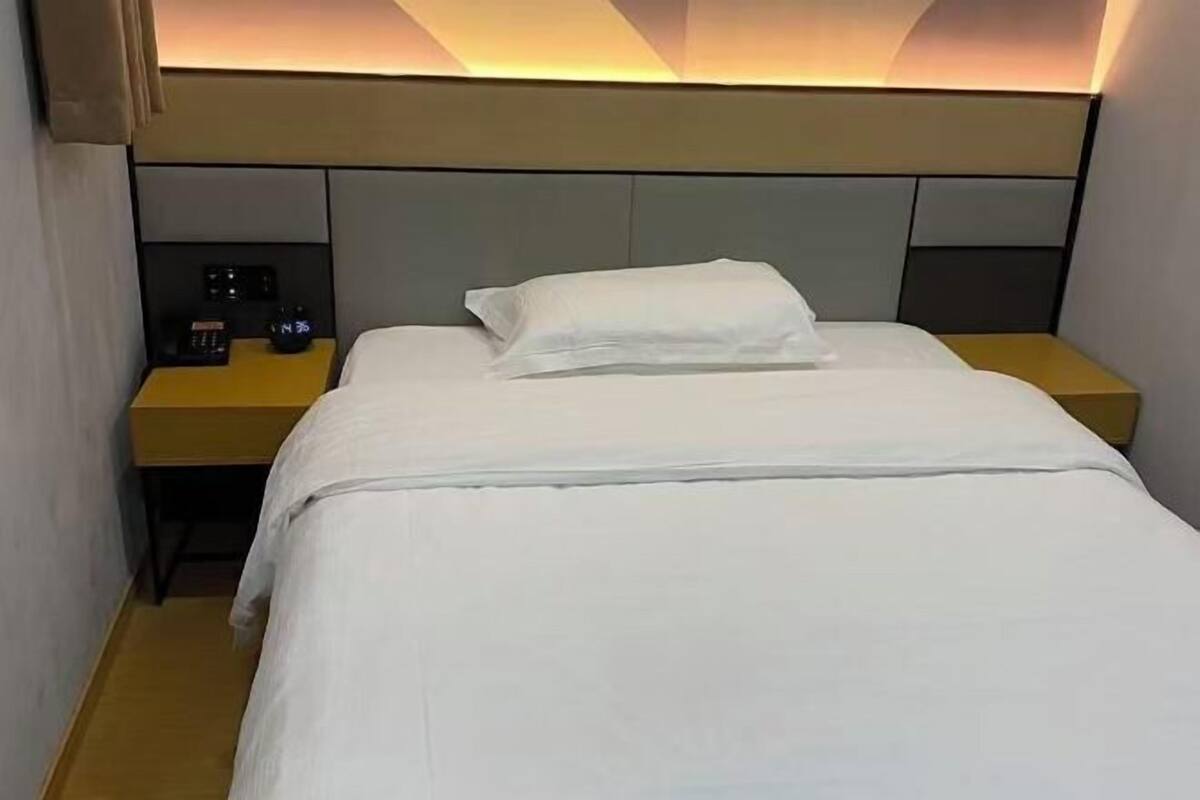 A hotel room with a bed, a nightstand with a clock, and a wall-mounted light fixture.