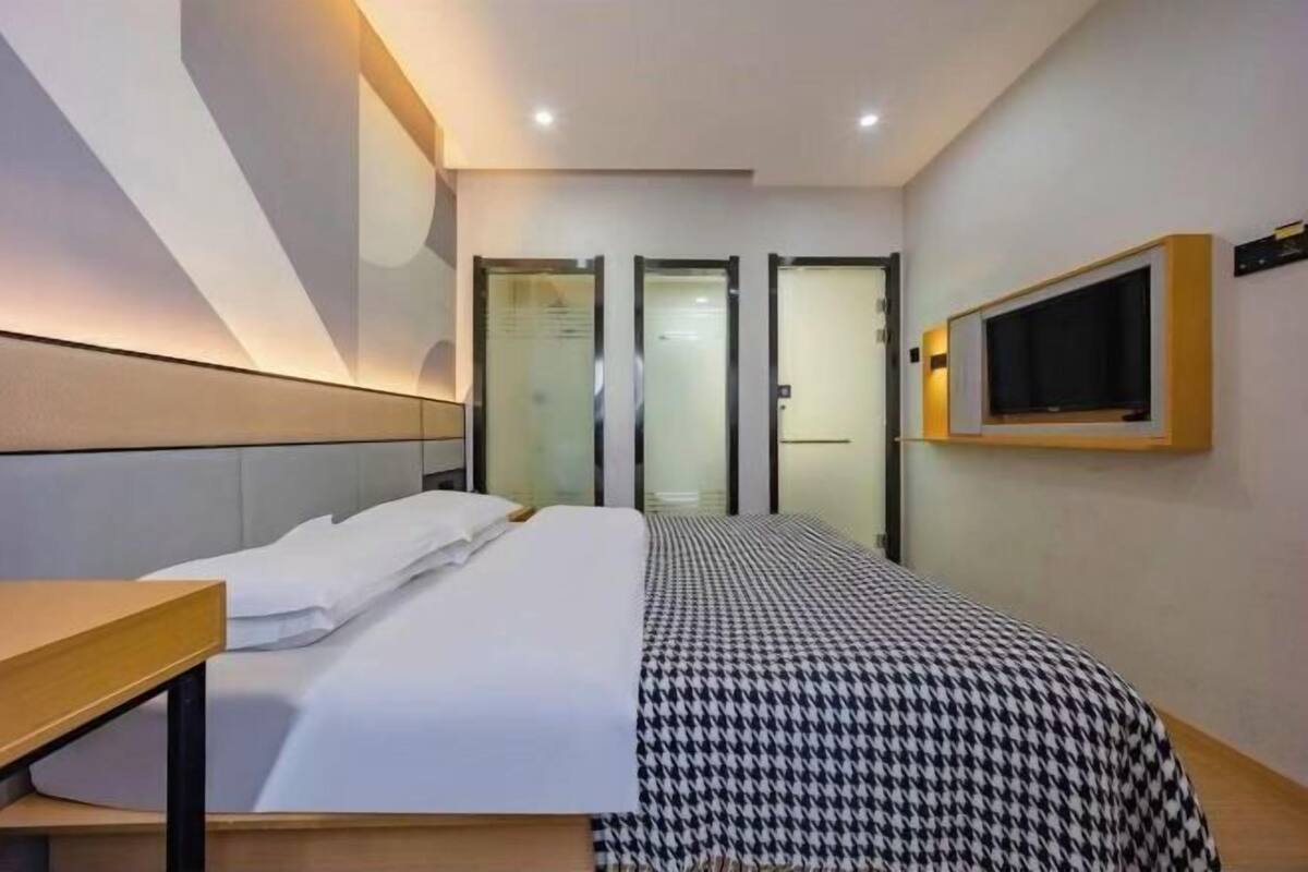 A hotel room with a bed, a TV mounted on the wall, and a desk.