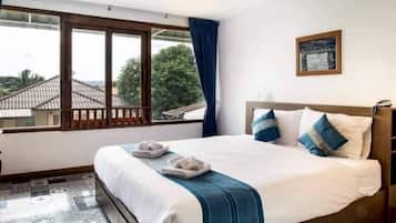 A hotel room with a large bed, a view through a window, and a painting on the wall.