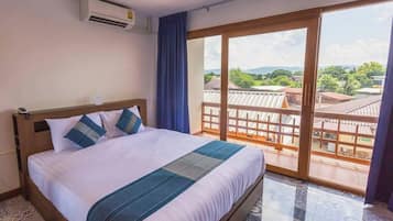 A hotel room with a large bed, a view of the outdoors through a sliding glass door, and an air conditioning unit on the wall.