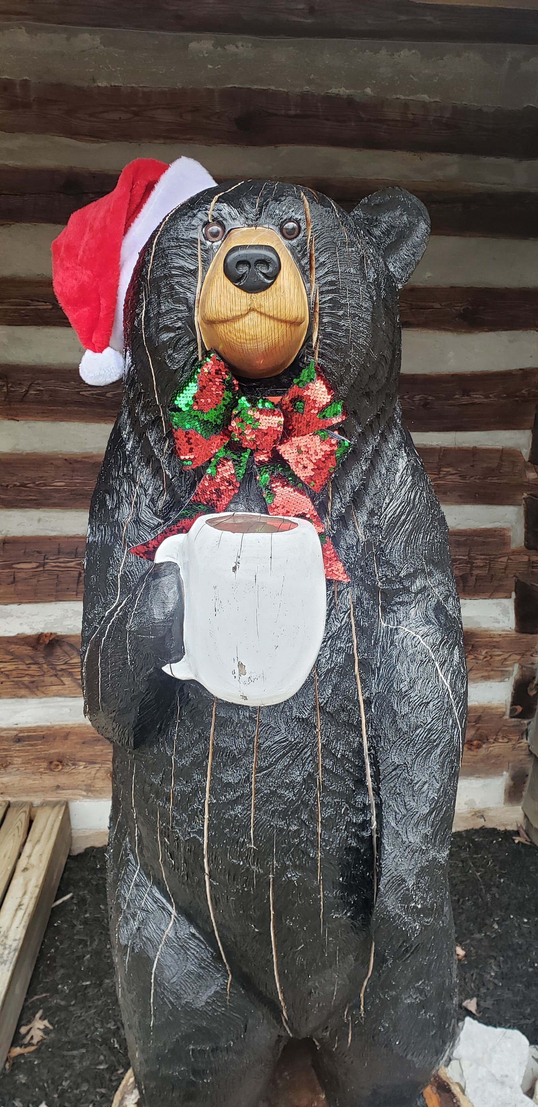 A bear statue wearing a Santa hat and holding a mug.