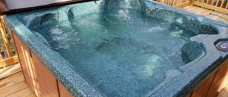 A hot tub on a wooden deck with a wooden railing in the background.