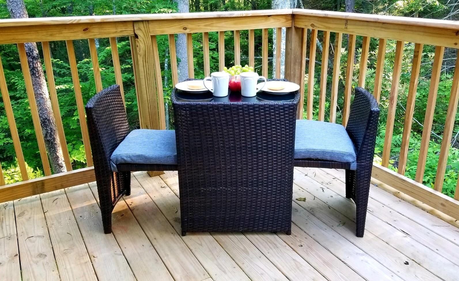 A wooden deck with a wicker table and two chairs, a plate, a pitcher, and a cup.