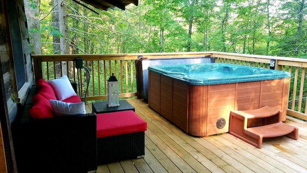 Eine Holzterrasse mit Whirlpool, einer gepolsterten Sitzecke und einer Laterne.