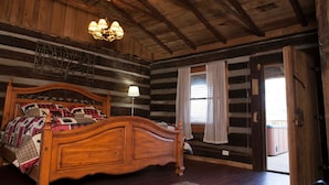 Ein Schlafzimmer in einer Blockhütte mit einem hölzernen Bett, einer Chandelieber und einem Fenster mit Vorhängen.