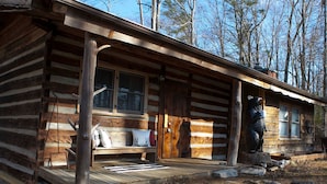 Eine Blockhütte mit Veranda, einer Bank und einer Bärenstatue.