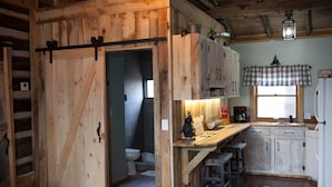 Eine rustikale Küche mit Holzsäulen, einer großen Holztür und einem karierten Fensterlamellentuch.