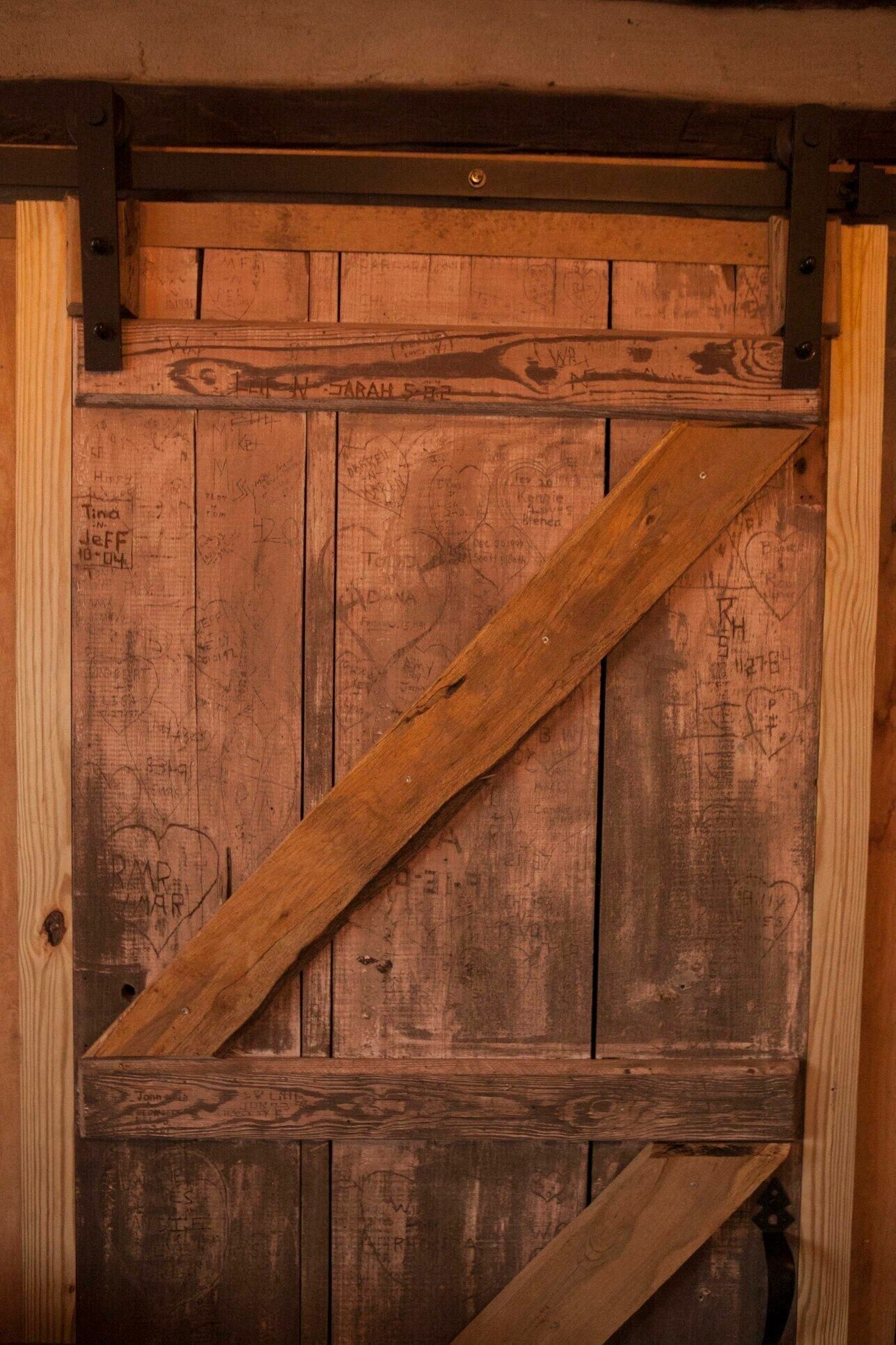 A rustic wooden door with a diagonal metal brace, featuring various handwritten notes and markings.