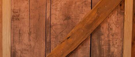 A rustic wooden door with a diagonal metal brace, featuring various handwritten notes and markings.