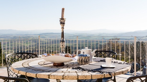 A round table with a candle, pastries, and a teapot on a balcony overlooking a mountainous landscape.