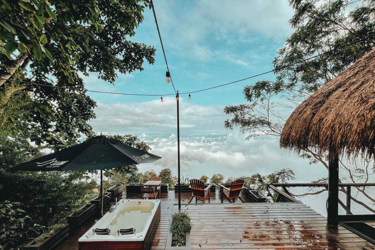 Une terrasse en bois avec un jacuzzi, des sièges d’extérieur et une structure dotée d’un toit de chaume.