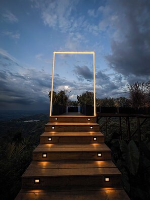 Eine hölzerne Treppe mit beleuchteten Stufen führt zu einer Umrandung vor bewölktem Himmel.