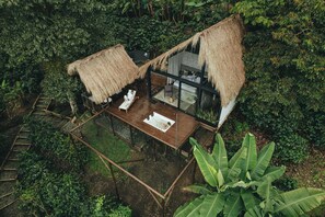 Ein Bungalow mit einem Reetdach und einer Glaseinfriedung, umgeben von dichtem tropischen Grün.