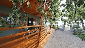 A wooden deck with a gravel path leading to a gate, surrounded by greenery and overlooking a body of water. - Mobile Home Smaragd (Biograd)