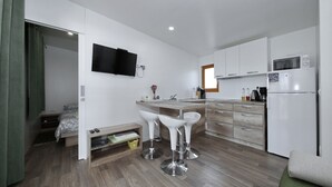 A compact kitchen with white cabinets, a microwave, and a refrigerator. There is a small dining area with two white bar stools. - Mobile Home Smaragd (Biograd)