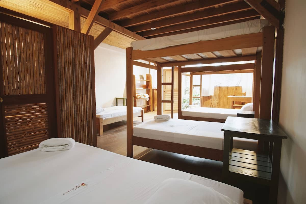 A room with two wooden bunk beds, a small table, and a view of the outdoors.