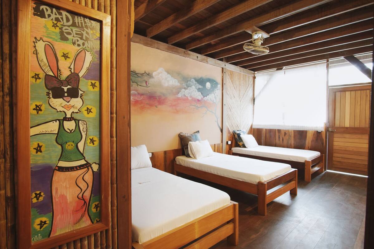 A room with two wooden beds, a wooden ceiling, and a framed artwork on the wall.