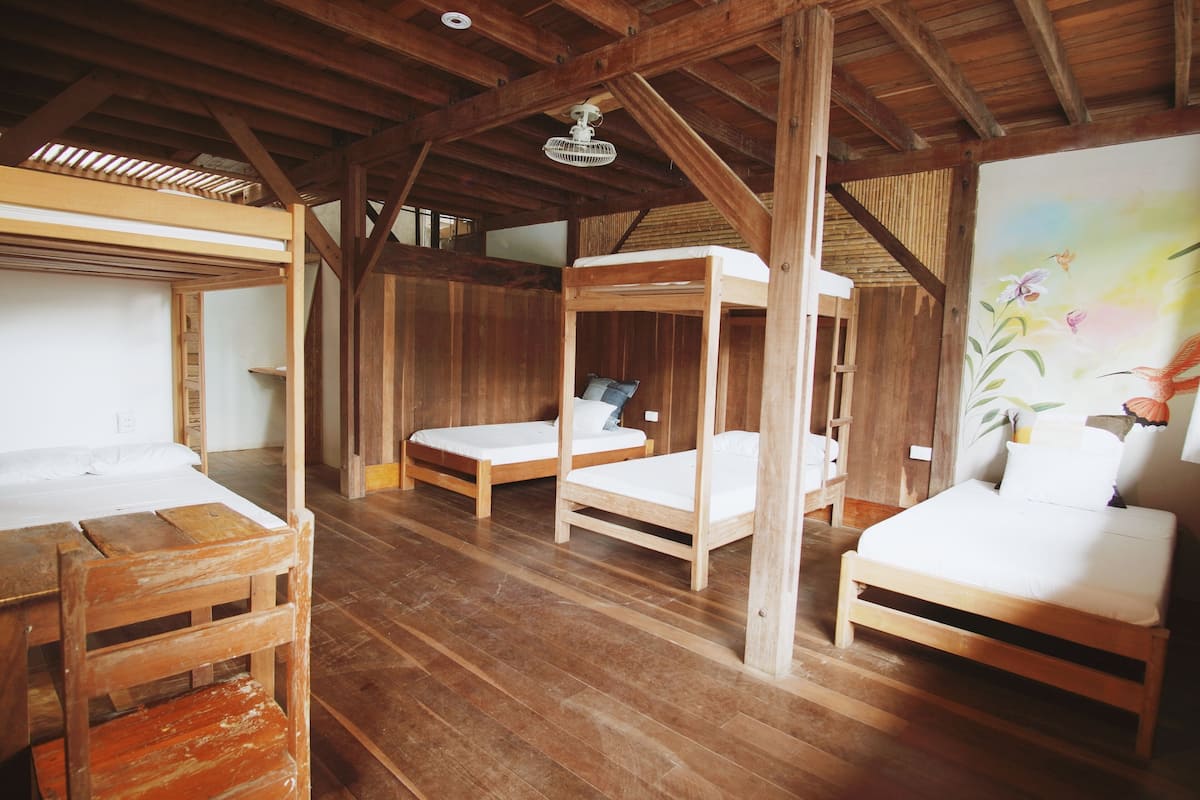 A rustic wooden room with four beds, a wooden table, and a ceiling fan.