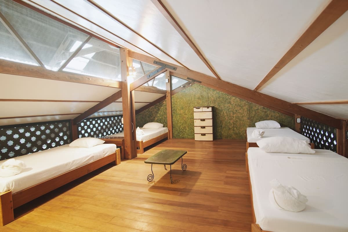 A dormitory-style room with wooden floors, bunk beds, a small table, and a wardrobe.